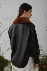 Campera corta de cuero color marrón con cuello de piel sintética color marrón claro, cierre frontal con botones a presión, mangas largas y bolsillos con solapa en el pecho.