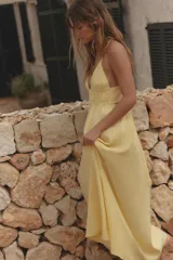 Vestido midi amarillo de tejido fluido con escote pico y tirantes finos cruzados en la espalda ajustables con lazada. Tiene detalle de elásticos bajo el pecho.