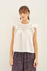 Camisa blanca de algodón con detalles de puntilla en el canesú, volados con terminación de puntilla en las mangas y cartera de botones en la parte superior de la espalda.