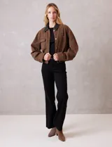 Campera de denim color marrón, con cuello de solapa en ecocuero negro. Cierre frontal con botones y bolsillos delanteros. Forro interno a tono.