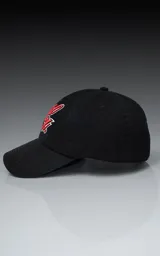 Gorra de gabardina color negro con visera curva y bordado frontal en hilo rojo con borde blanco que simula una letra 'L' estilizada. Posee ajuste trasero de velcro.