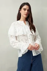 Camisa negra semitransparente de encaje bordado con diseño geométrico. Tiene silueta fluida, mangas largas y volados en el frente y los hombros.