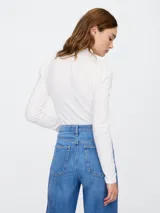 Remera blanca de cuello alto con mangas largas abullonadas en los hombros.