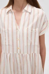 Vestido corto a la rodilla, color blanco con rayas verticales color naranja, de corte holgado, con cuello camisero, mangas cortas y cierre frontal con botones.