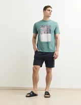 Remera color petróleo de manga corta con estampa de un edificio y texto en el frente.