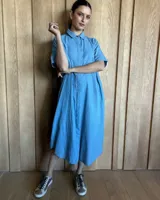 Vestido túnica celeste de lino con rayas verticales blancas, corte recto, cuello camisero y mangas cortas.