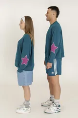 Buzo azul petróleo de corte holgado con cuello redondo y manga larga. Estampa de estrella fucsia en el antebrazo.