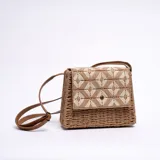 Bandolera de paja color marrón con solapa con diseño geométrico en beige y marrón. Tiene correa larga de cuero sintético marrón.