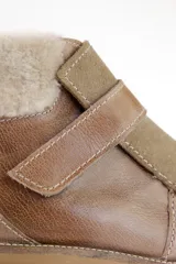 Bota corta de cuero color marrón con puntera y empeine de gamuza color beige. Tiene cuello de piel sintética color crema, cierre con velcro y suela track.