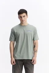 Remera de manga corta color verde menta, con escote redondo y fit regular. Presenta un estampado en la espalda con la frase "NO RULES! BREAK THE RULES" y un diseño abstracto en tonos azules y blancos.