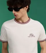 Remera blanca de algodón, corte baby tee, con cuello redondo y mangas cortas con ribete doble en bordó. Estampa pequeña con texto "The Staff" en el pecho.