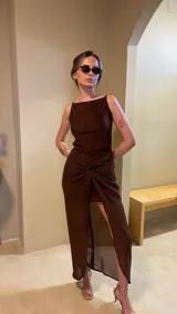 Vestido largo marrón con breteles finos, corte ajustado en la parte superior y falda con abertura lateral y detalle de nudo en la cintura.