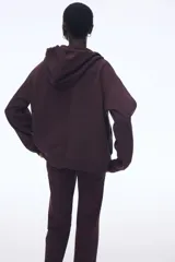 Campera con capucha color borgoña, con cierre frontal y bolsillos tipo canguro. Confeccionada en felpa con interior cepillado suave, hombros caídos, capucha forrada con cordón para ajustar y puños y bajo en punto acanalado.