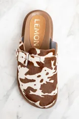 Zuecos con capellada de cuero con estampado animal print de vaca, base marrón con suela track y hebilla metálica ajustable.