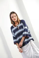 Remera de algodón y poliéster a rayas horizontales rojas y azul marino sobre fondo crudo. Tiene cuello tipo polo con botones, mangas amplias y corte oversized.