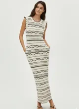 Vestido largo de punto color crudo con rayas horizontales negras, sin mangas y cuello redondo. Tiene bolsillos laterales y detalles de volados en los hombros y ruedo.