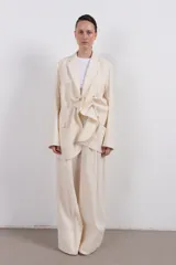 Blazer color crema de corte amplio con diseño asimétrico y detalle de nudo frontal.