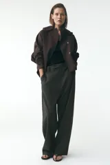 Trench corto color negro, con cuello solapa y capucha desmontable mediante botones. Manga larga tipo murciélago acabada en trabilla ajustable. Bolsillos laterales. Forro interior combinado. Cierre frontal con botones. Tejido repelente al agua.