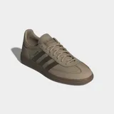 Zapatillas Adidas Handball Spezial de corte bajo, con parte superior de ante en tono beige claro y tres franjas laterales en verde oliva. Presentan puntera en T y suela de goma color café. La inscripción "SPEZIAL" se encuentra en el lateral en color oscuro.
