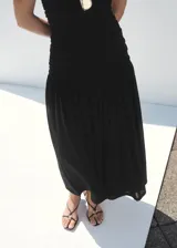 Vestido midi negro sin mangas, con cuello redondo, fruncidos laterales y diseño evasé.