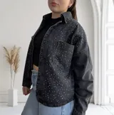 Campera de jean negra con tachas plateadas, corte recto, cuello camisero y cierre frontal con botones.
