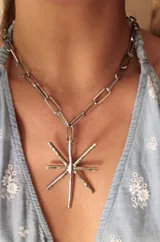 Collar plateado con cadena de eslabones grandes y dije en forma de estrella con puntas. El dije tiene incrustaciones de strass.