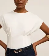 Blusa blanca de algodón con cuello redondo y mangas cortas. Presenta pliegues delanteros y traseros con efecto corsetado.