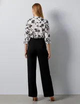 Blusa de gasa blanca con estampado floral en negro. Presenta cuello a la base con escote en V y abertura con botones. Las mangas son largas y se pueden ajustar a tres cuartos.