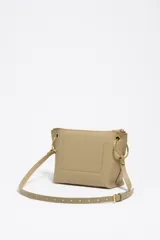 Bolso bandolera de piel vacuna negra, con forma trapezoidal y estructura rígida. Posee asa regulable, cierre de cremallera, bolsillo interior y charm decorativo con borlas en tonos tierra y dorado.