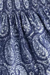 Vestido midi de algodón con estampado paisley en tonos azules y blancos. Tiene breteles finos ajustables y escote recto con frunces. El cuerpo es fruncido con costura elástica en el busto y la falda tiene un leve vuelo.