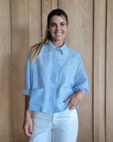 Camisa celeste a rayas verticales blancas, de corte holgado, manga 3/4 y cuello camisero.