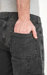 Bermuda de denim color gris oscuro con efecto desgastado, corte oversize estilo carpintero y bolsillo lateral.