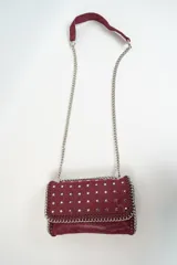 Cartera de cuero sintético color borgoña, con tachas plateadas en forma de estrella y correa de cadena plateada.