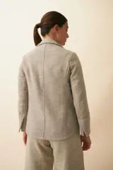 Chaqueta color crema de corte recto con cuello, solapa y bolsillos ojal. Forro solo en las mangas y terminaciones envivadas. Esquinas redondeadas y mangas con corte en puño que permiten transformarla en manga 3/4. Más larga en la espalda que en la delantera. Abrochadura con dos botones.