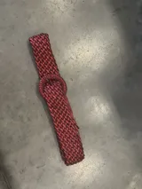 Cinturón elástico trenzado color rojo con hebilla circular forrada.