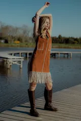 Vestido corto marrón de gamuza sintética, sin mangas, con escote en V y detalle de flecos en el ruedo. Presenta apliques bordados en el frente y laterales.