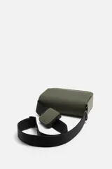 Bandolera negra con acabado engomado y textura acanalada. Tiene un compartimento principal con cierre de solapa y botón a presión, un bolsillo interior con cremallera y un monedero cuadrado en la correa. La correa de hombro es ajustable.
