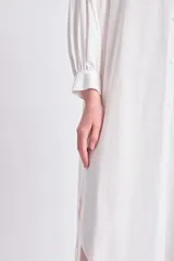 Vestido camisero largo color blanco, con cuello mao, abotonadura frontal y mangas largas abullonadas con puños camiseros.