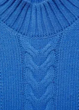 Sweater color crema de punto trenzado con cuello alto.