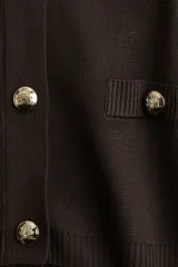 Saco corto marrón de punto fino suave, entallado y de manga corta con cuello redondo, botonadura frontal y bolsillos delanteros decorativos con botón.