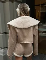 Conjunto color beige compuesto por chaqueta corta con cuello de piel sintética y short con cierre frontal.