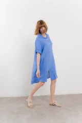 Vestido camisero corto color verde oliva, confeccionado en lino 100%. Tiene botones en la parte delantera, cuello camisero, mangas cortas con botón para arremangar y bolsillos laterales.