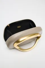 Bolso formato caja color crema con asa de cadena dorada para usar como bandolera. Cierre metálico dorado.
