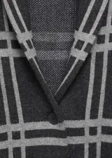 Abrigo largo de punto grueso con estampado de cuadros grises sobre fondo negro. Tiene cuello con solapa, cierre frontal con botones y dos bolsillos de parche.