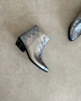 Botín de cuero vacuno color bronce con puntera y caña en cuero negro. Diseño con borde superior en zigzag y taco de madera.