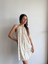 Vestido corto color crudo con estampado de líneas verticales marrones, cuello redondo con frunce y tirantes con lazo.