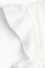 Top blanco de manga corta con escote redondo y abertura en V con tiras para atar. Presenta canesú con inserciones de encaje y costura fruncida con volados. Corte holgado.