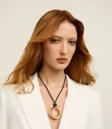 Collar corto con cordón negro ajustable y un colgante circular grueso en tono dorado. El diseño destaca por su aro de metal reciclado con acabado brillante.