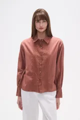 Camisa color terracota con cuello camisero, botones frontales y detalle de broderie en el pecho. De corte holgado y manga larga con puños.