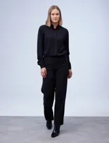 Pantalón de vestir negro de tiro alto, corte wide leg y pierna ancha. Presenta detalles de botones decorativos en la parte frontal superior y bolsillos laterales.